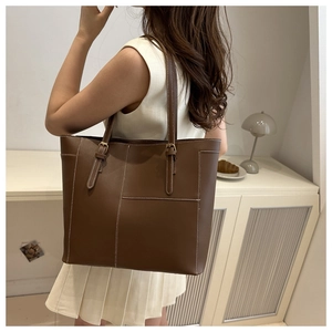 Detail of dark brown tote bag featuring contrast white stitching and buckle accents