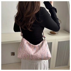Detail of pink shoulder bag featuring quilted texture and colorful embroidered stripes