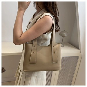 Minimalist beige faux leather tote bag with stylish metal rivet accents and classic retro style