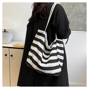 Close-up of a black and white striped canvas tote bag worn with a black wool coat