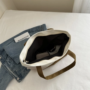 Grand sac cabas en toile crème avec anses marron et fermeture éclair sur un lit