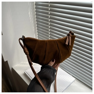 Close-up of pleated dark brown suede hobo bag with knotted strap detail in soft lighting
