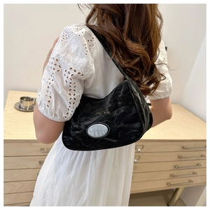 Detailed view of black ruched shoulder bag with silver logo on white lace dress