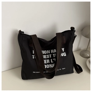 Detail of black nylon tote bag with brown straps and white lettering on minimalist desk