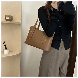 Detail of a brown leather tote bag featuring gold stud accents and fine shoulder straps