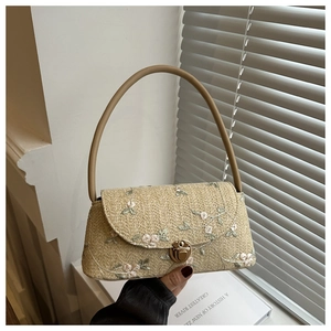Detail of woven straw shoulder bag featuring floral embroidery and golden metal swivel lock