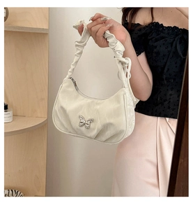 Close-up of white pleated handbag featuring a silver butterfly buckle and scrunchie strap