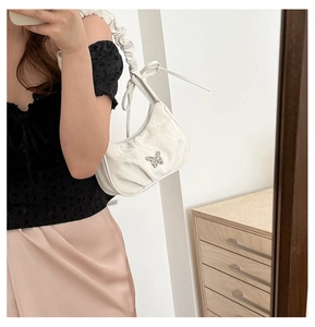 Close-up of white pleated shoulder bag featuring a silver butterfly buckle and scrunchie strap