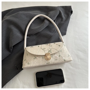 Detail of floral embroidery and gold twist lock on the woven straw underarm bag