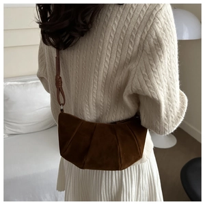Detail of dark brown suede shoulder bag with pleats on model in cream knit sweater