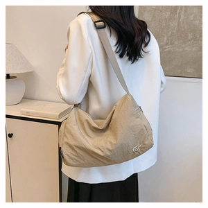Detail view of khaki nylon crescent bag with adjustable strap worn over white blazer