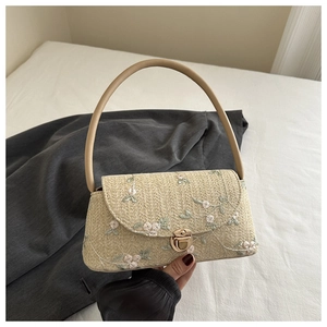 Detail of floral lace embroidery on a woven straw shoulder bag with metallic clasp