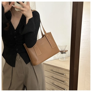 Brown leather tote bag styled with casual earth-tone outfit in a lifestyle setting