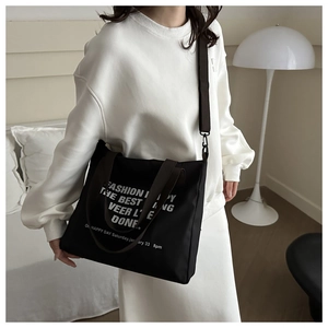 Detail of black canvas tote bag with white lettering and brown adjustable shoulder strap