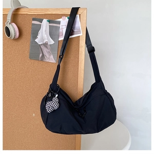 Détail du sac croissant en nylon noir avec breloque à carreaux sur un tableau en liège