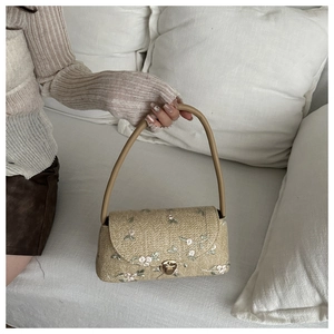 Detail of beige straw bag featuring delicate floral embroidery and brown leather handle