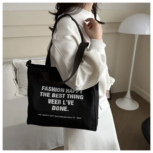 Black canvas tote bag featuring white artistic typography shown in a lifestyle home setting