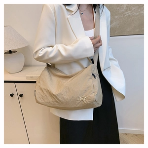Detail of beige nylon crossbody bag with metal logo and adjustable strap on a model