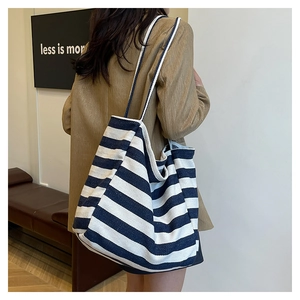 Detail of blue and white striped canvas tote bag worn on shoulder in a minimalist setting