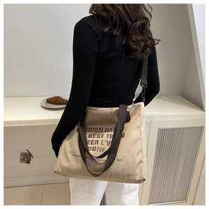 Detail of a beige canvas tote bag with brown straps and Fashion Happy text print
