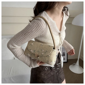 Detail of straw shoulder bag featuring floral embroidery and elegant metal twist lock