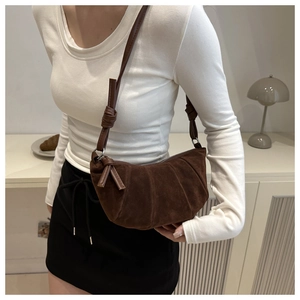 Close-up of dark brown suede crescent bag with decorative knot detail on strap