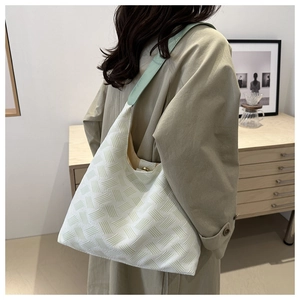 Detail of white moon bag with green strap and textured woven surface on shoulder