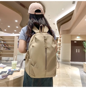 Detail of minimalist beige backpack showing side water bottle pocket and woven zipper pull