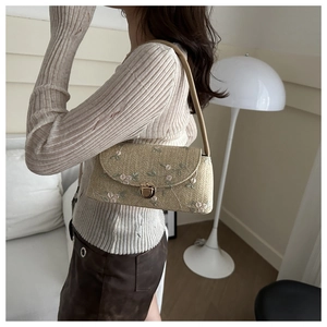 Close-up of beige woven shoulder bag featuring delicate floral embroidery and metal clasp
