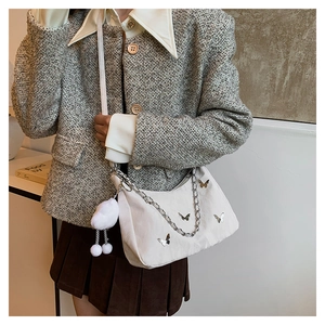 Detail of cream tote bag with butterfly metal accents, chain strap and cloud pendant