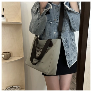 Detail view of large canvas tote bag with adjustable brown straps and black letter print