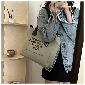 Close-up of a large green canvas tote bag with brown text and leather handles