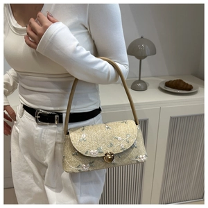 Detail of straw shoulder bag featuring floral lace embroidery and gold metal clasp