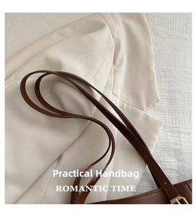 Close-up of adjustable brown leather shoulder strap with gold buckle on a tote bag