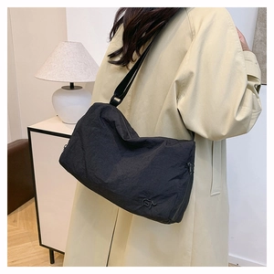 Detail of black pleated fabric texture on a large crossbody bag with subtle logo embroidery