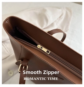 Detail of smooth golden metal zipper closure on large brown faux leather tote bag