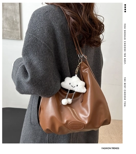 Detail of a brown leather hobo bag with an oval logo and a cute white plush cloud charm