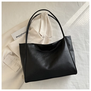 Gros plan d'un sac cabas en cuir noir à texture souple et fines anses sur un tailleur