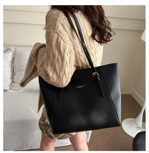Detail of black leather tote bag with shoulder strap and metal brand logo patch