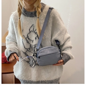 Detail of blue nylon crossbody bag featuring an adjustable strap and plush bear charm