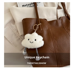 Plush white cloud charm with embroidered smile on a brown leather tote bag
