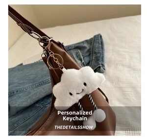 Close-up of white plush cloud charm with smiley face on a brown leather tote bag