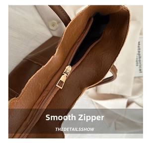 Close-up of the smooth metal zipper and leather texture on a brown tote bag