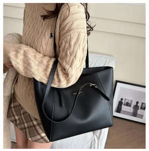 Close-up of a large black leather tote bag featuring a square fashion label and slim straps