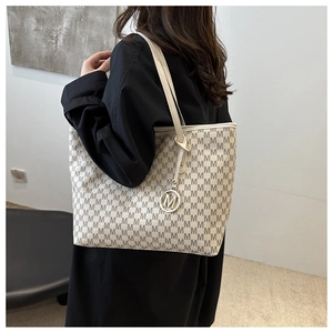 Detail shot of cream tote bag featuring dark grey M-monogram pattern and gold pendant