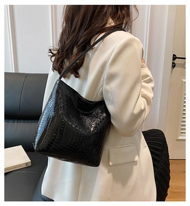 Black crocodile pattern tote bag shown over the shoulder in a minimalist indoor setting