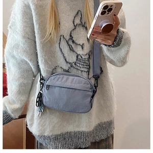 Detail shot of light blue nylon crossbody bag with zipper pockets and chain accessory