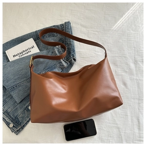 Flat lay of caramel leather hobo bag with wide strap next to a denim jacket and book