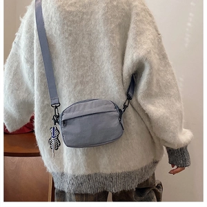 Side view of minimalist nylon crossbody bag in dusty blue with checkered bear charm