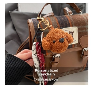Close-up of brown plush teddy dog charm with braided cord on a plaid crossbody bag
